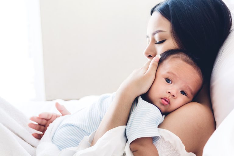 Mother holding baby in her arms and kiss in a white bedroom.Love