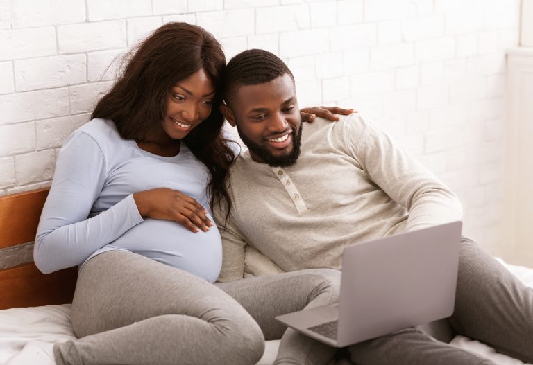 Happy pregnant couple looking at a computer screen smiling