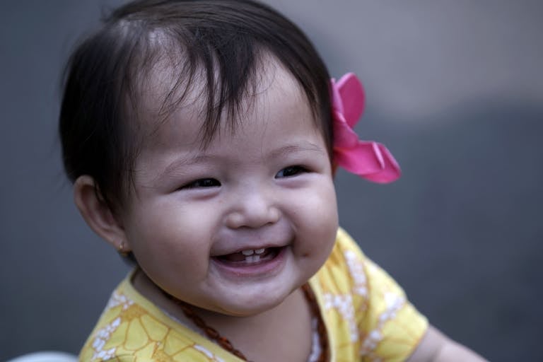Smiling baby girl with pink hair bow and yellow dress, capturing pure joy.